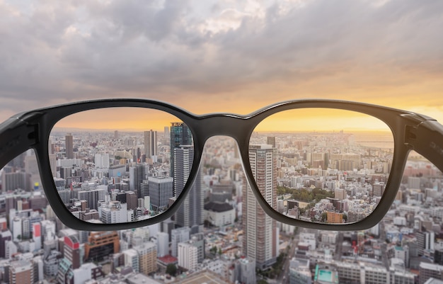 Photo looking through eyeglasses to city sunset view, focused on lens with blurry background