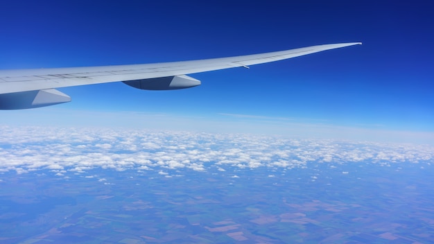 Looking thru airplane 's window seeing wing of airplane , white clouds , blue sky and land of Moscow , Russia