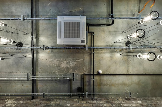 Looking up on gray concrete ceiling with halogen spots and edison lamps in loft office room with air conditioning and orange ventilation pipe