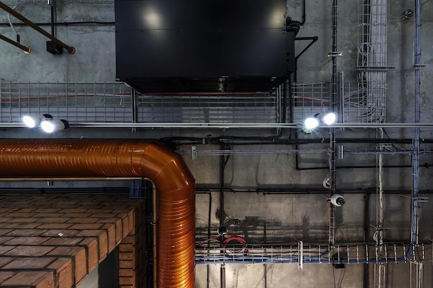 Photo looking up on gray concrete ceiling with halogen spots and edison lamps in loft office room with air conditioning and orange ventilation pipe