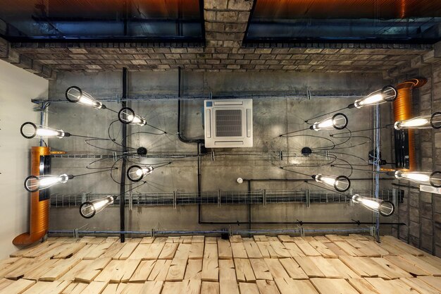 Looking up on gray concrete ceiling with halogen spots and edison lamps in loft office room with air conditioning and orange ventilation pipe