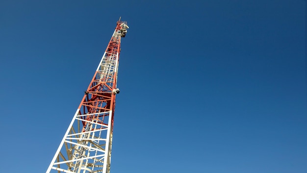 Alzando lo sguardo alla piccola torre delle telecomunicazioni rossa e bianca, con i piatti di comunicazione in cima. sfondo tecnologico astratto, spazio per il testo a destra.