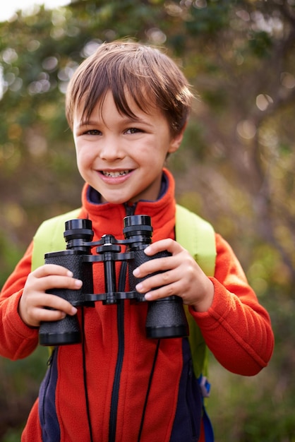 Photo on the lookout for my next adventure portrait of a happy young boy out in the woods with a pair of binoculars