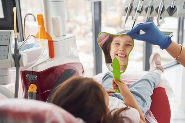 Looks into the mirror Little girl visiting dentist in clinic Conception of stomatology