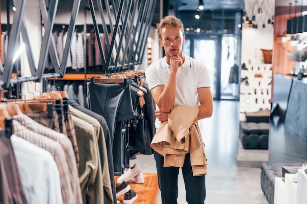 ジャケットを探す新しい服を着たモダンな店の若い男男性のためのエレガントで高価な服