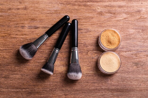 Loose compact mineral powder for face and a brushes for powder and visage on wooden background eco