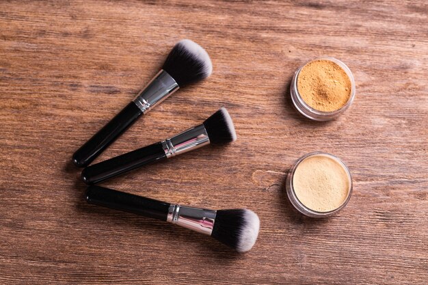 Loose compact mineral powder for face and a brushes for powder and visage on wooden background eco