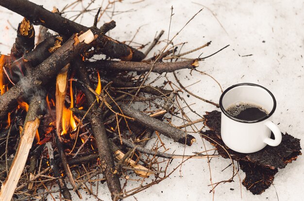 Lopende mok met koffie dichtbij het kampvuur. Concept wandeling, wandeling, reis in de winter