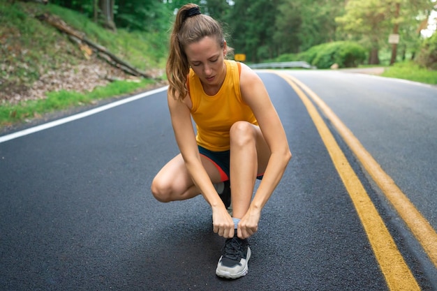 Loper vrouw veters strikken om te joggen rennen op bosweg