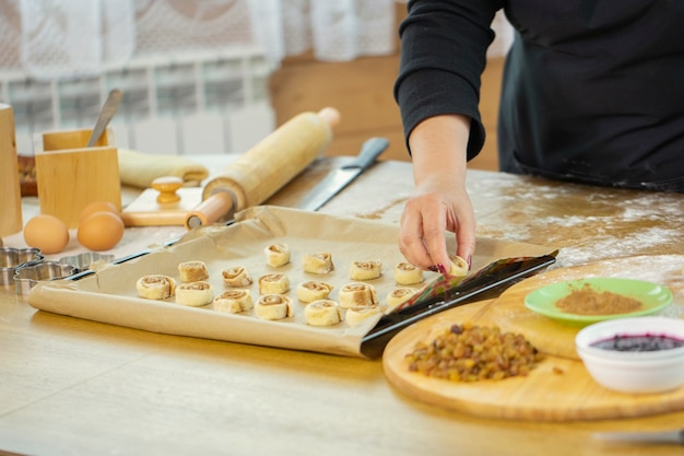 ÃÂ¡lose up female baker hand puts cinnamon buns with spices and cocoa on baking sheet with parchment paper