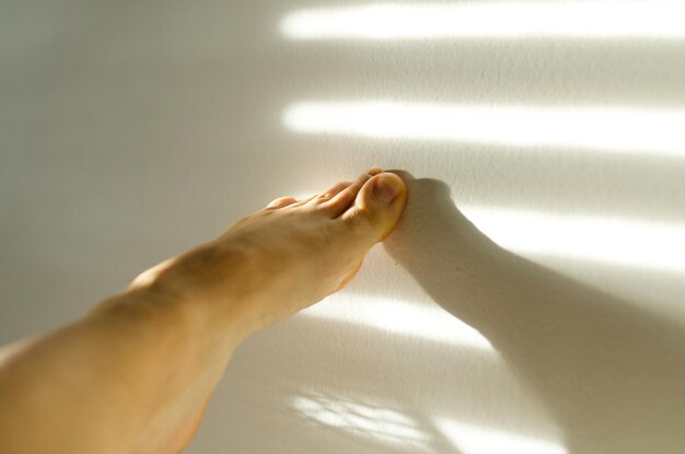 Lose up of a female legs, toes against white wall at cozy home\
in sunset light. shadows at the wall.