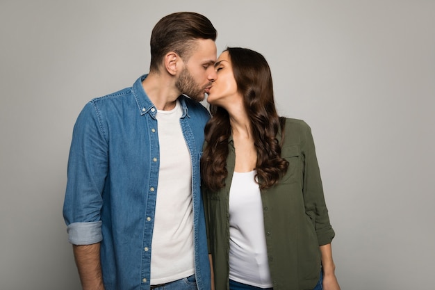 Ð¡lose-up photo of a charming lady with chestnut hair, who is kissing her handsome boyfriend in the cheek, while hugging him from the back.