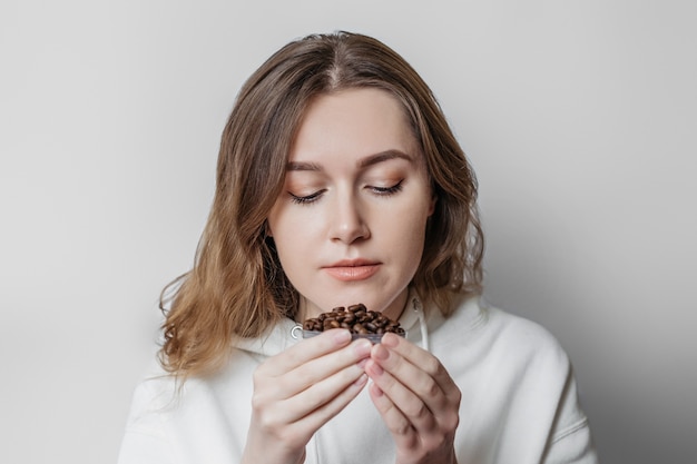 Loss of smell. Close up portrait of caucasian young woman sniffing coffee grains isolated. Coronavirus concept