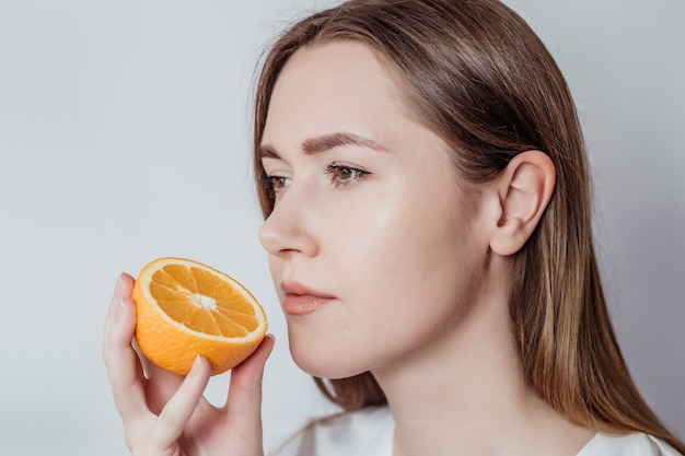 Концепция потери запаха. Крупным планом портрет кавказской молодой женщины, держащей апельсин возле ее носа, изолированные