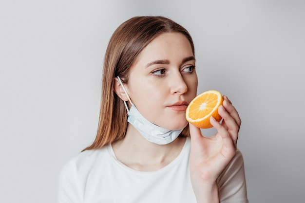 Loss of smell concept. Portrait of caucasian young woman holding an orange near her nose isolated