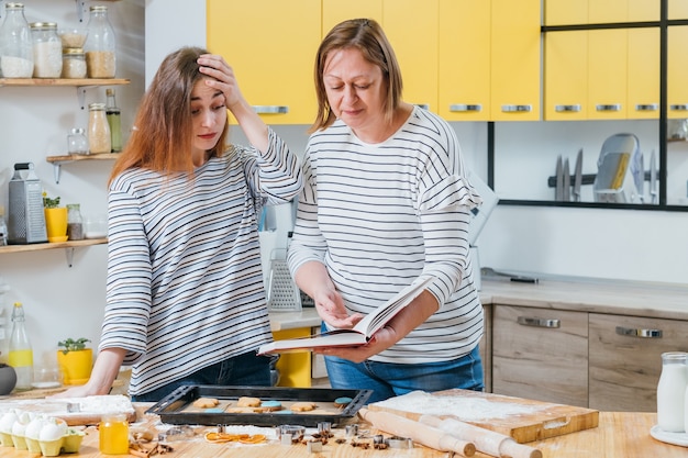 Lossere chef. Moeder houdt kookboek vast en wijst op de fout die haar dochter heeft gemaakt bij het koken van koekjes.