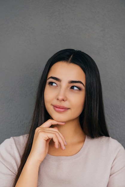 Lost in thoughts. Thoughtful young woman holding hand on chin and looking away