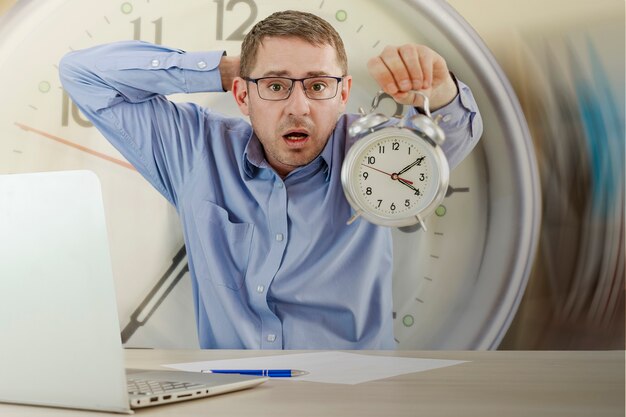 Lost time concept An office worker holding his head holds out an alarm clock