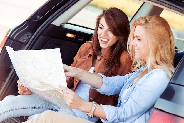 Lost with map two young woman friends in car