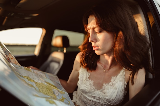 Perso giovane donna seduta nella sua macchina in campagna e guardando la mappa