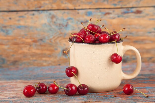 A lot of berries of a sweet cherry in a mug on an old woody background