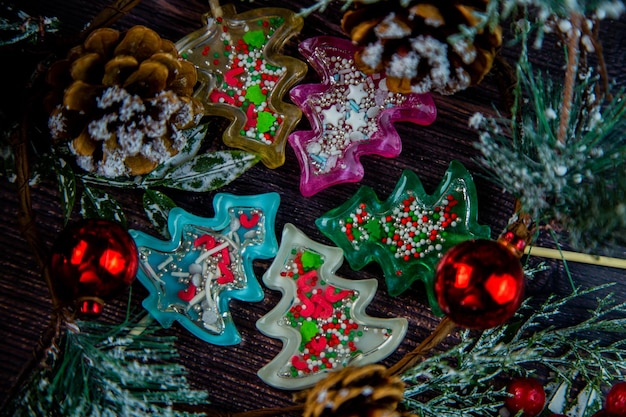 A lot of christmas trees of lollipops of different colors lie in a circle on a wooden table surround...