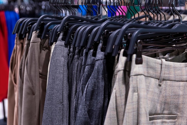 A lot of classic trousers of the autumn-winter collection on hangers in the store. Close-up. Selective focus.