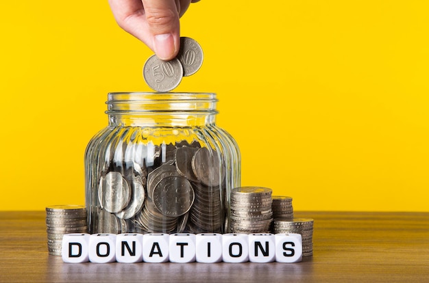 A lot coins in glass money jar with yellow background saving for donations concept