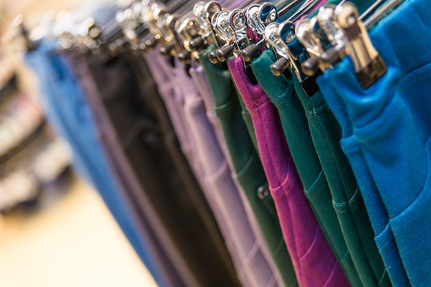 Много цветных джинсовых брюк висит на вешалках в магазине одежды