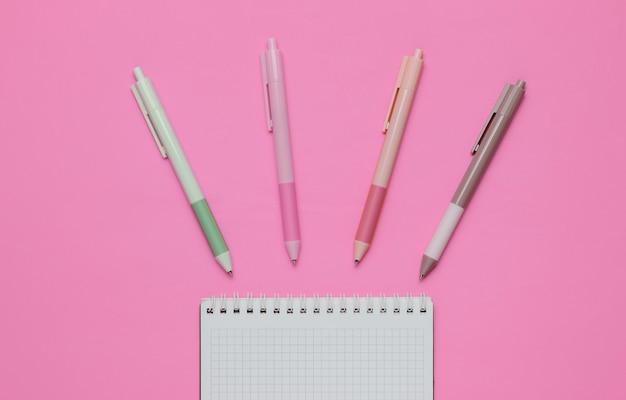 ピンクの背景にノートブックのクローズアップと色付きのペンがたくさん。上面図