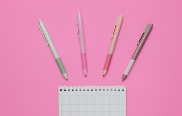 A lot of colored pens with notebook close-up on pink background. Top view