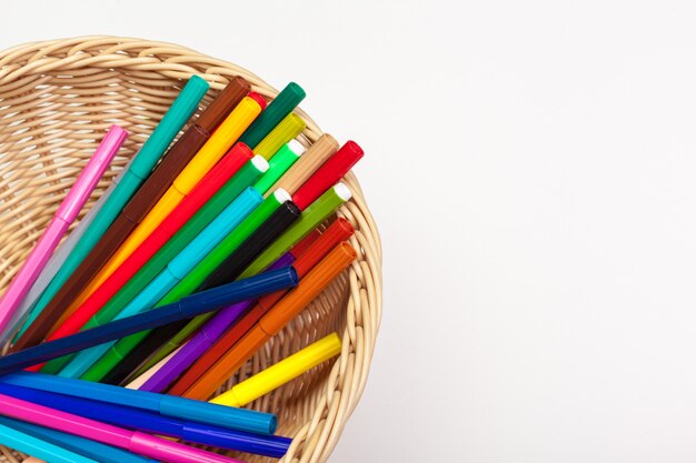 Lot of colorful markers in a wooden basket on white