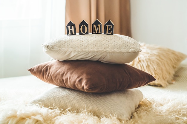 A lot of decorative cozy pillows and the inscription HOME. In the home interior on the bed. Spring in the home interior. HOME concept