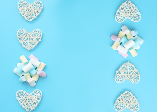 A lot of delicious white yellow blue and pink marshmallows  with white rattan hearts on blue background