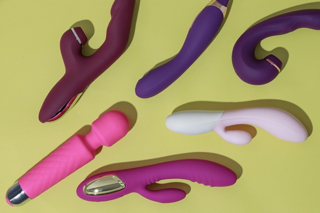 A lot of different dildo vibrators on yellow background with shadows sex toy for adult