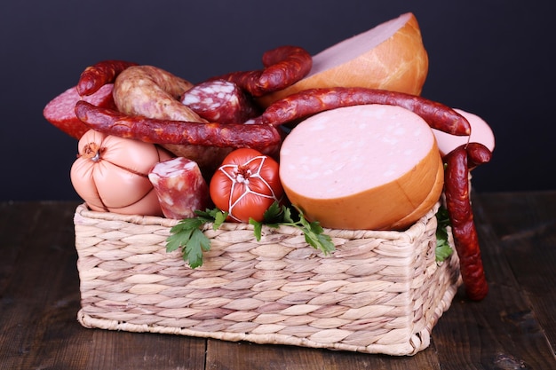 Lot of different sausages in basket on wooden table on black background