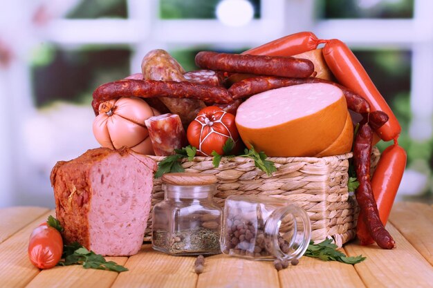 Lot of different sausages in basket on wooden table on window background