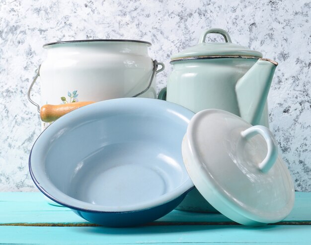 Photo a lot of enameled dishes on a blue table on a white concrete wall background. retro style cookware