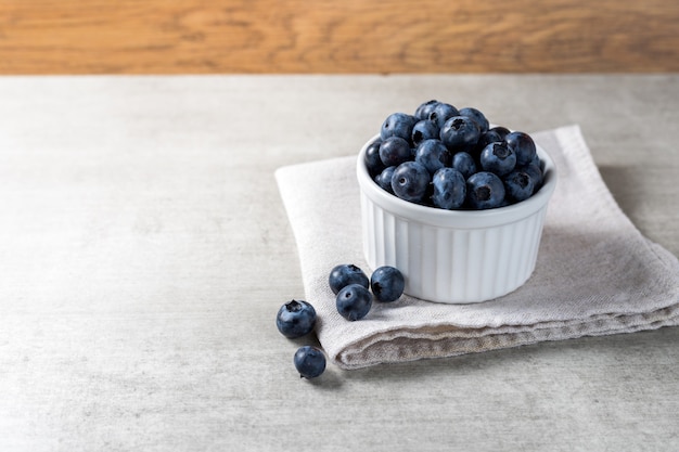 Lot of fresh delicious blueberries on a white pot over a wooden table.