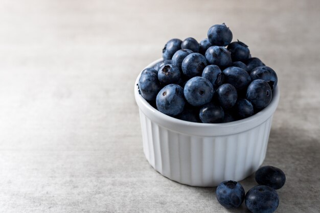 Lot of fresh delicious blueberries on a white pot over a wooden table.