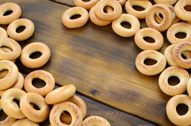 A lot of fresh yellow bagels lie on the surface of the old dark wood