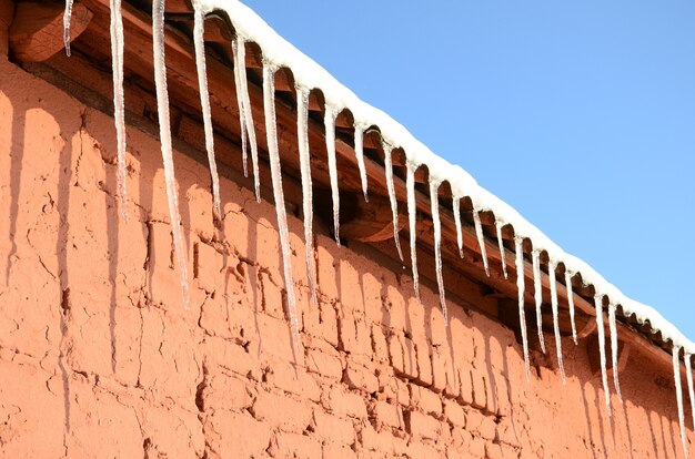 A lot of long icicles hang under the roof of a red brick building