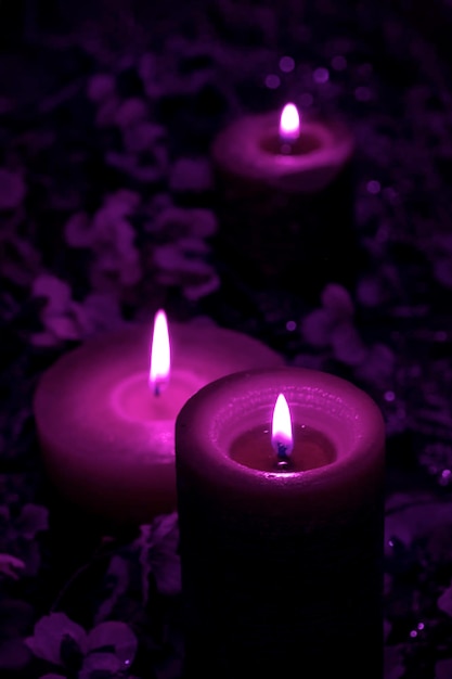 A lot of magic purple and velvet violet colours candles burn on the blue background with flowers.