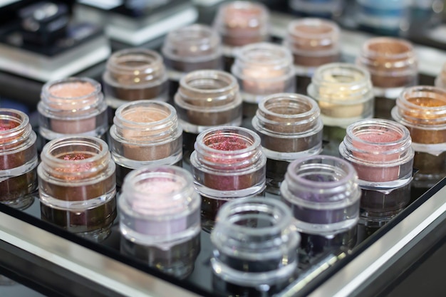 A lot of multi-colored eye shadows with glitter in jars on a black background.