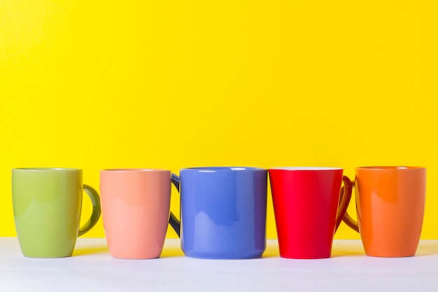 A lot of multicolored cups of coffee or tea on a yellow background. the concept of a friendly company, a large family, meeting friends for a cup of tea or coffee