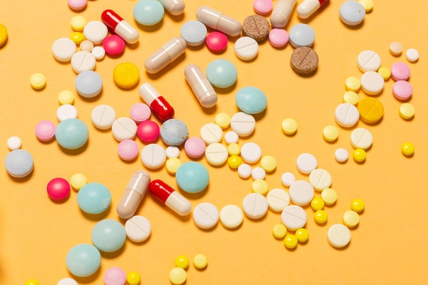 A lot of multicolored pills and capsules orange background as concept of addiction from medicine