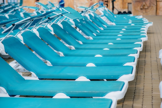 В солнечный день у бассейна в отеле стоит много новых красивых синих лежаков. Счастливого отпуска. Летний отдых и туризм.