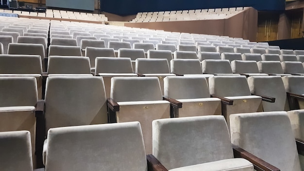 A lot of old beige upholstered chairs without people in the hall for performances and films. Background from many chairs in the stands in a concert hall or theater.