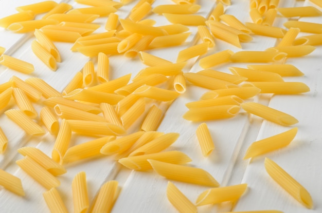 A lot of pasta is scattered on a white wooden table. The concept of eating.