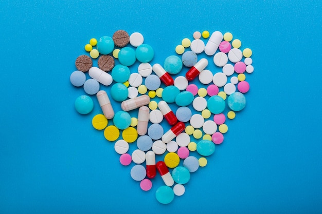 A lot of pills on the blue background in a heart shape as a symbol of medical treatment